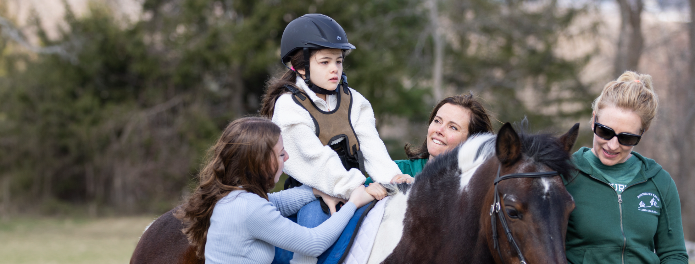 Mia riding her horse alongside the stable staff